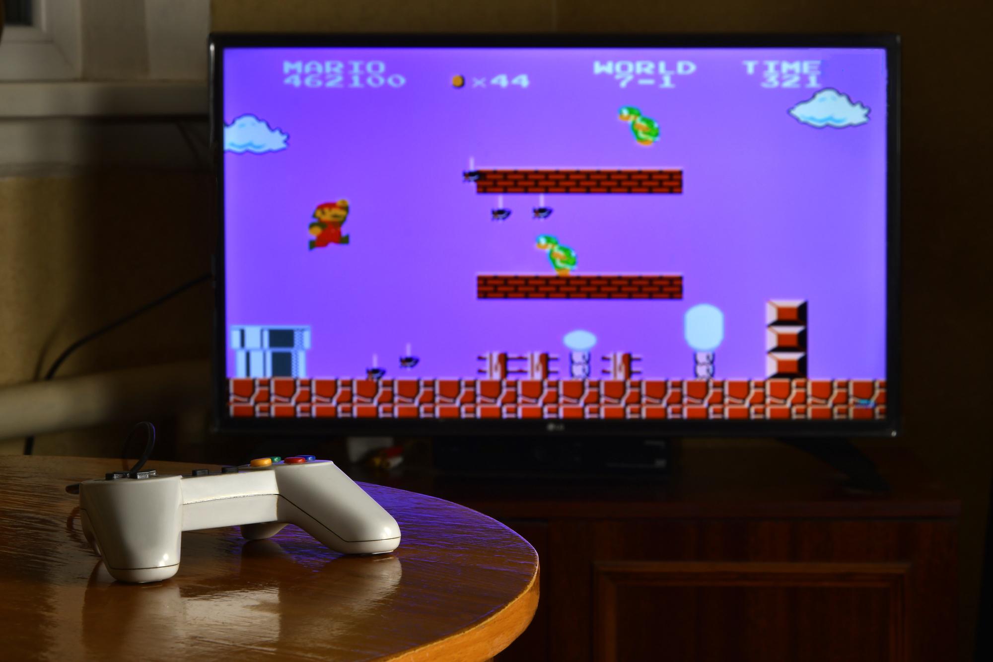 Videospiel-Controller auf einem Tisch mit dem Spiel Super Mario Bros auf einem Bildschirm im Hintergrund